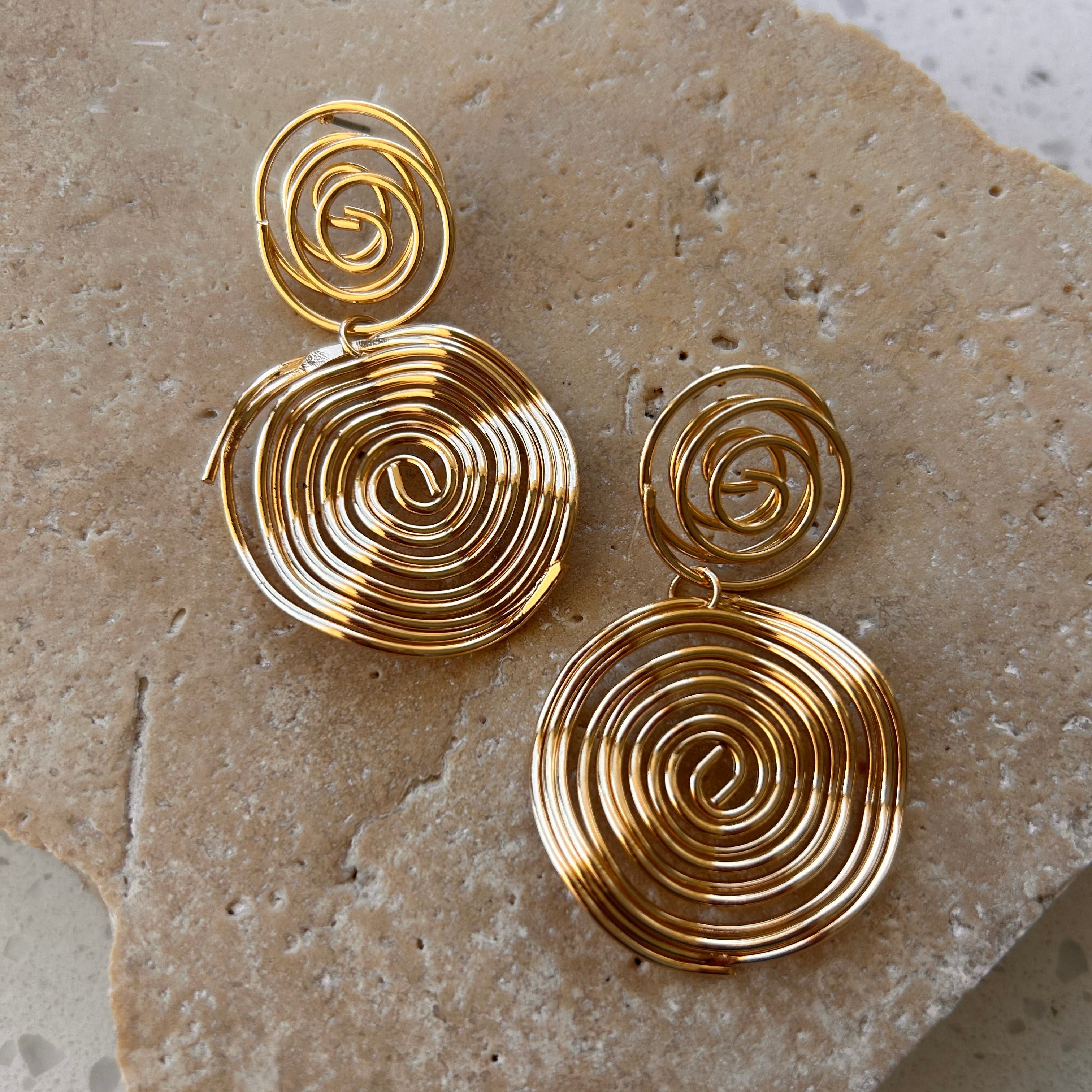 Pair of gold spiral earrings on a textured stone surface bohemian style costume jewellery in Australia 
