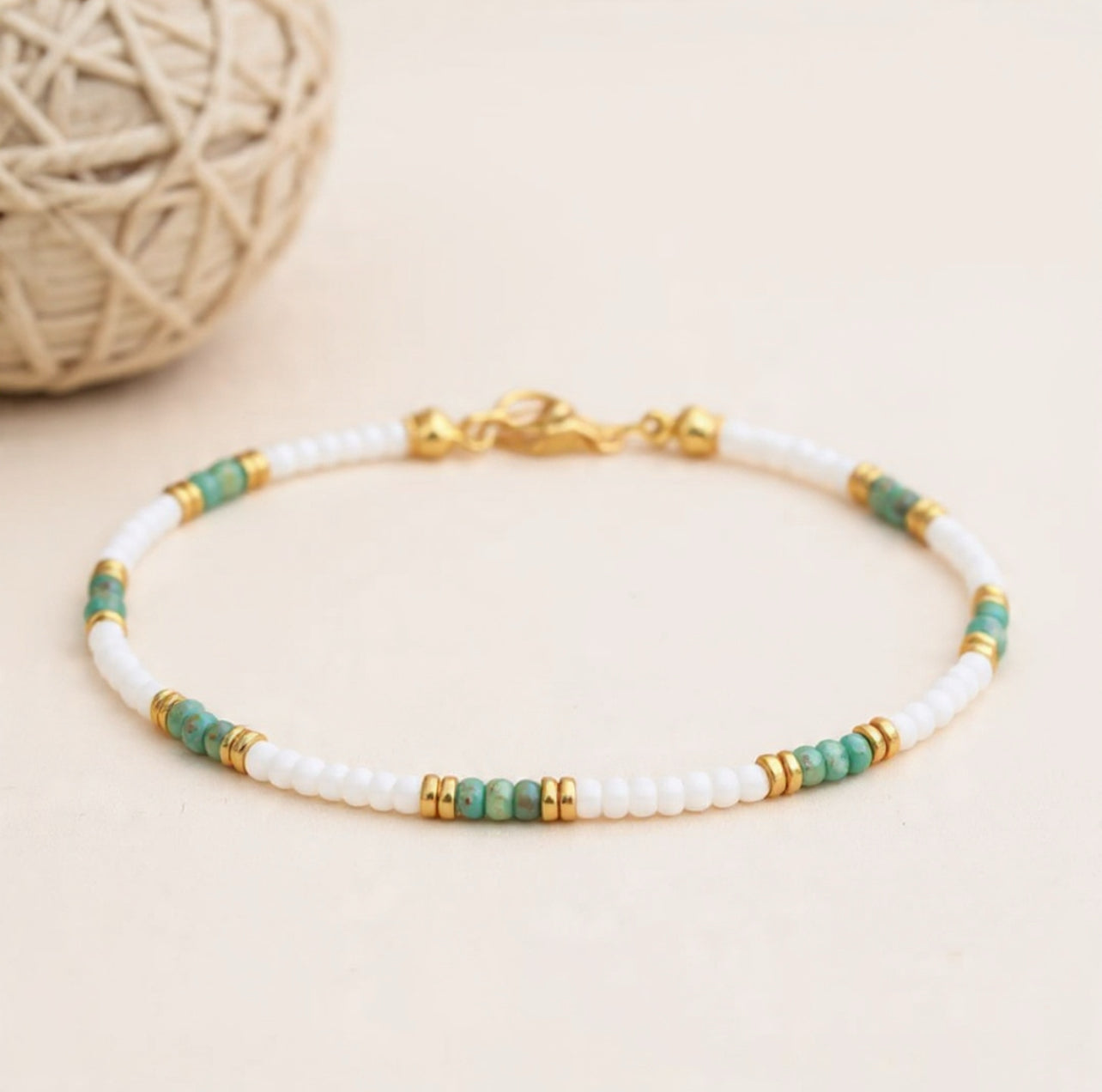 Boho ankle Bracelet with white, green, and gold beads on a beige background