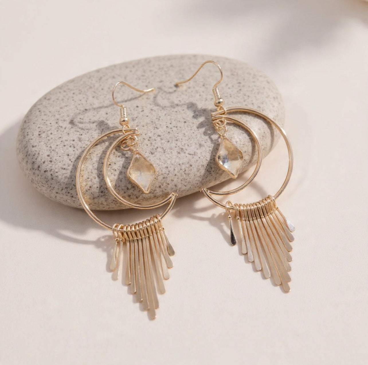 Gold hoop earrings with fringe details on a stone surface
