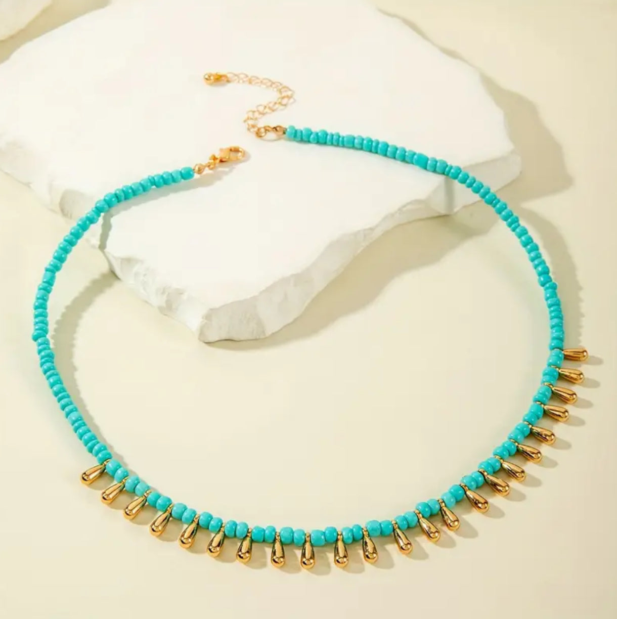 Turquoise beaded necklace with gold accents on a beige background
